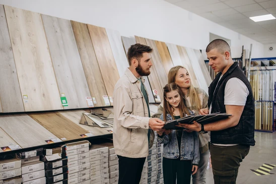 Un homme examine des plans d'architecture sur une table de travail, tenant un &eacute;chantillon de parquet