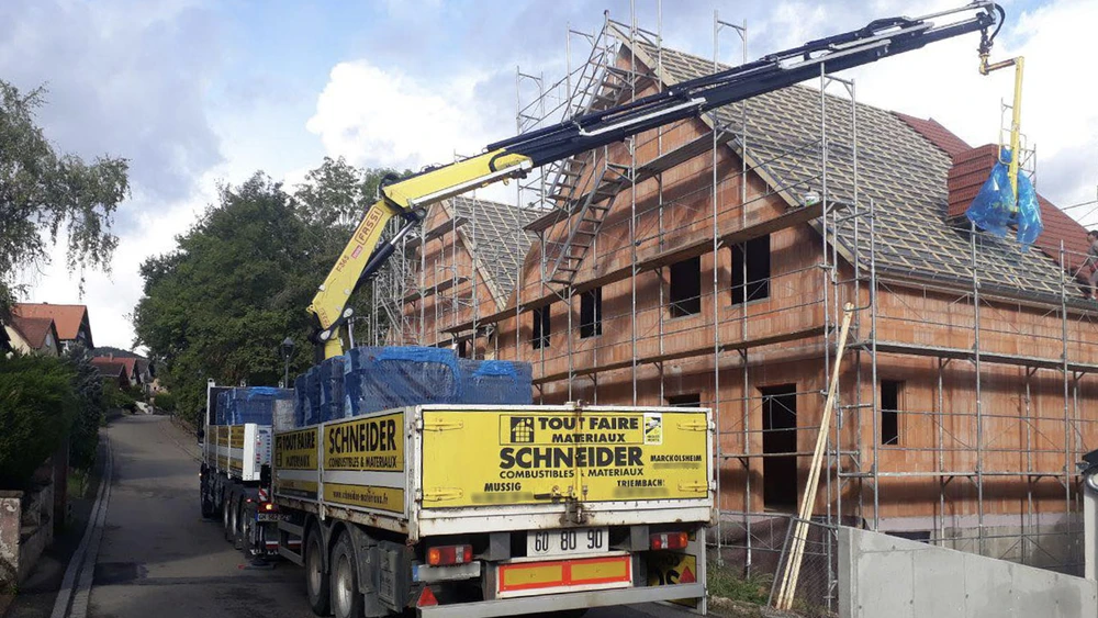 Scène extérieure d'un dépôt de matériaux de construction avec camion-grue Volvo blanc transportant des éléments préfabriqués en béton empilés